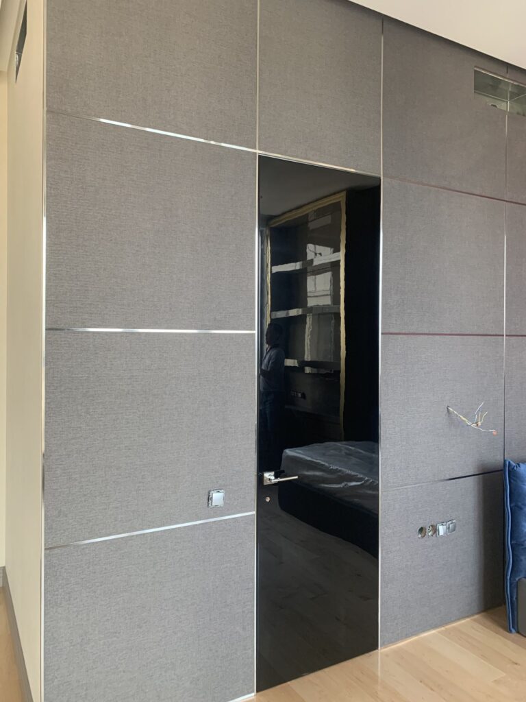 Глянцевая черная дверь и текстильные серые стеновые панели в убранстве спальни