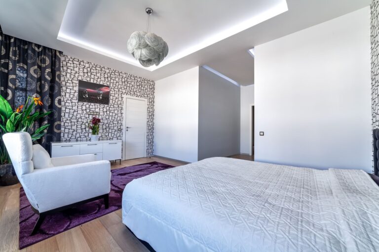 Спальня с двухуровневым потолком в светодиодной подсветке и светло-серой люстрой